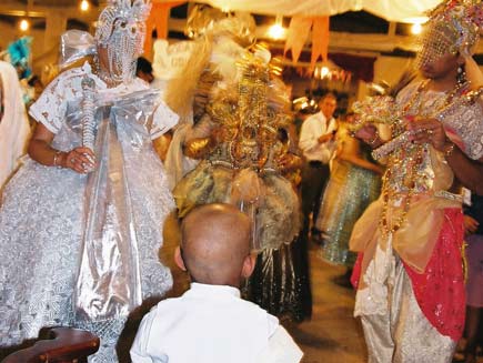 Initiation ceremony. The back of a boy can be seen, as he looks on at people dressed as brightly coloured orixa.
