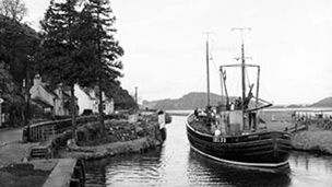 Fishing boat passes small village of Bellanoch as it enters Crinan Canal.