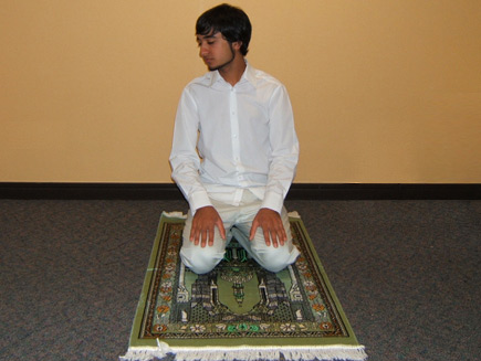 A man sits on his heels with his hands on his thighs, his head facing towards his right