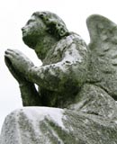 Grave marker in the shape of a stone angel with hands held together in prayer
