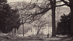 Black and white view of Blair Castle seen through trees from the graveyard of St Bride's Church.