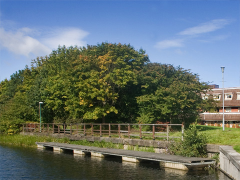Colour view of canal side, with trees and late 20th Century hotel behind.