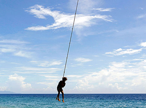 A girl swings on a rope attached to a palm tree on Bonegi beach.