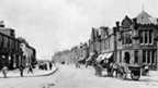 Black and white view of a couple with a pram and dog walking along a winding, coastal footpath. In the background are trees and the tall, cylindrical Battle of Largs Monument.