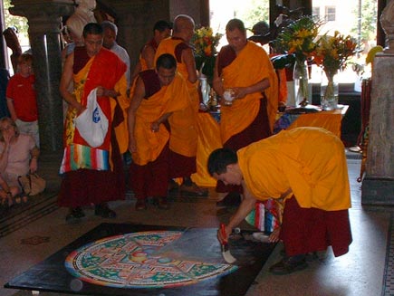 A quarter of the mandala has now gone. A monk is sweeping the sand up using a large paintbrush, working from the outside edge inwards