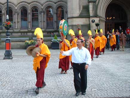 The monks leave Manchester Town Hall in procession, still wearing their full regalia. They are singing and playing cymbals and drums