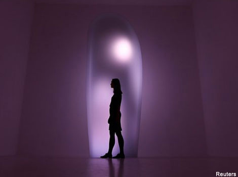 Silhouette of a woman standing in front of a standing stone sculpture.