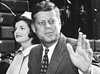 Senator John F Kennedy sits atop a car with his wife Jacqueline Kennedy, waving during a parade moving along Broadway, New York City (19 October 1960)