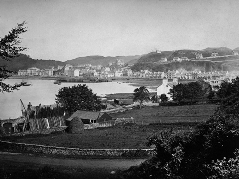 Black and white view of Oban, looking across farmland to the bay, harbour and town.