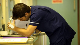 A male nurse leans over a desk looking tired