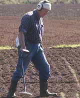 a metal detectorist scanning a field with his detector