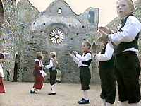 Boys and girls in traditional outfits dancing in rows inside the ruins of a cathedral